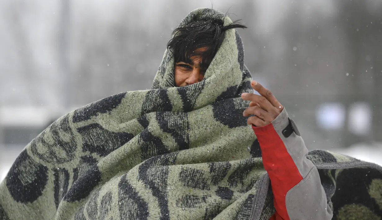Seorang migran membungkus dirinya dengan selimut saat berjalan melewati salju di kamp Lipa, barat daya Bosnia, Sabtu (26/12/2020). Para imigran membungkus tubuh mereka dalam balutan selimut dan kantong tidur untuk melindungi diri dari serangan angin dingin yang menusuk. (AP Photo/Kemal Softic)
