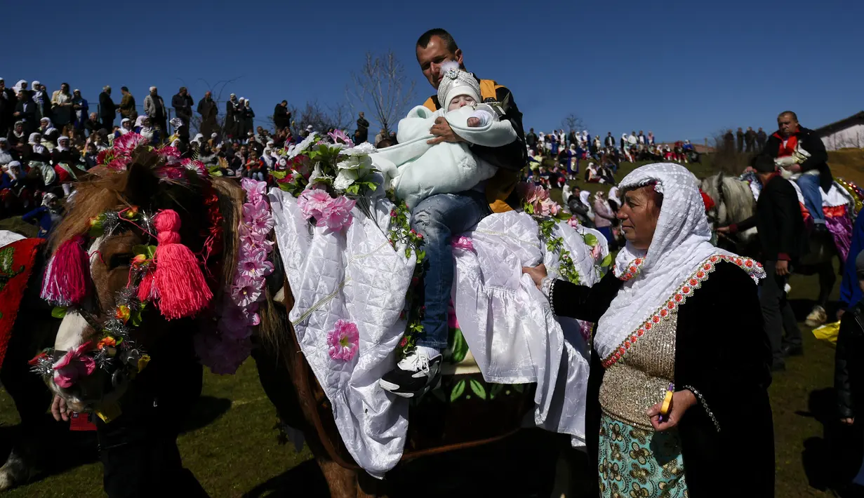 Pria muslim Bulgaria menggendong putra mereka saat menunggang kuda selama upacara sunat massal untuk anak laki-laki di Desa Ribnovo, 11 April 2021. Penduduk Desa Ribnovo adalah muslim berbahasa Bulgaria, kadang-kadang disebut sebagai "Pomaks" atau "orang yang menderita". (Nikolay DOYCHINOV/AFP)