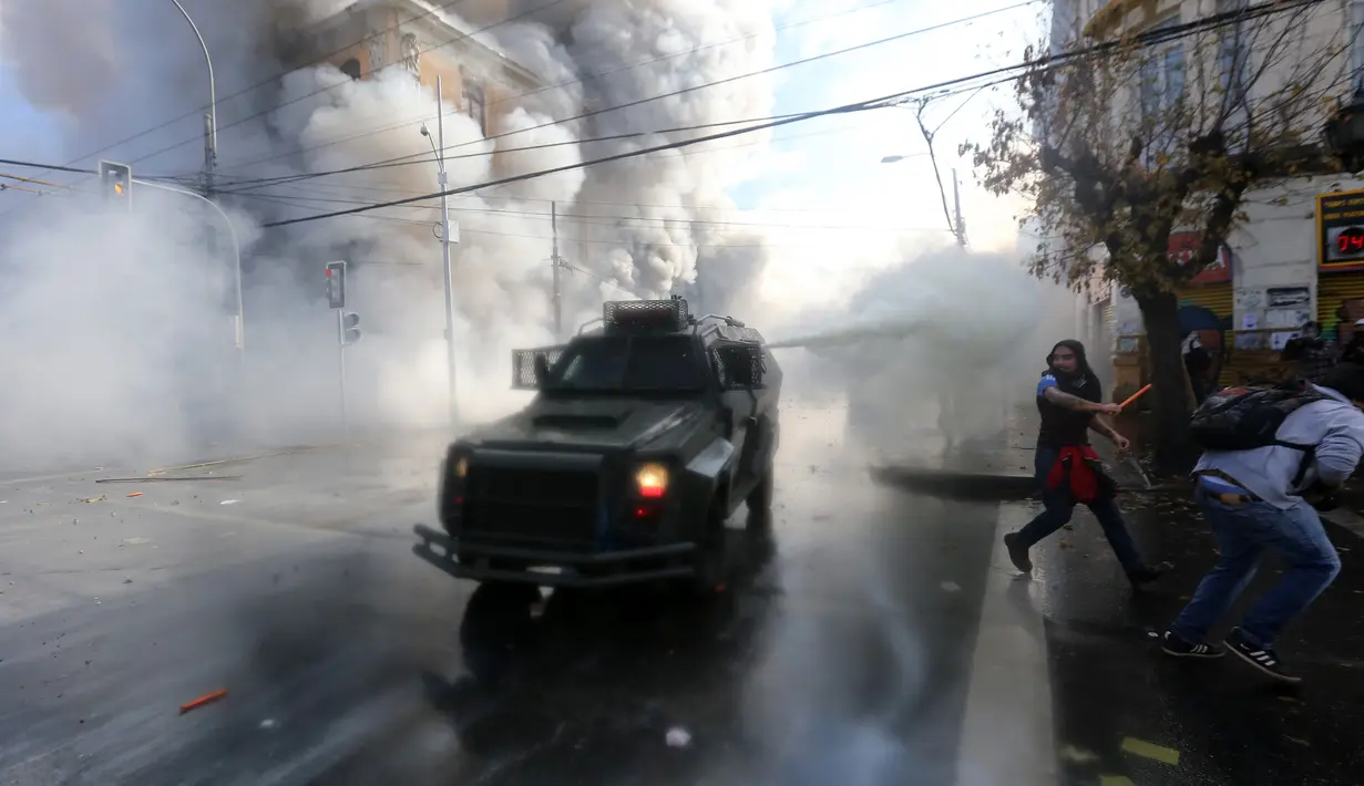 Polisi menyemprotkan gas air mata untuk membubarkan unjuk rasa yang berlangsung ricuh di sekitar Kongres di Valparaiso, Chili. Sabtu (21/5). (AFP Photo/Claudio Reyes)