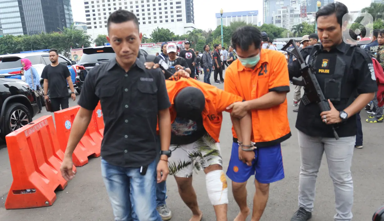 Petugas membawa sejumlah tersangka tindak kejahatan dalam rilis akhir tahun di Balai Polda Metro Jaya, Jumat (27/12/2019). Polisi juga menampilkan barang bukti ganja dengan total mencapai 1 ton yang diamankan dari setiap polres dan wilayah hukum Polda Metro Jaya. (Liputan6.com/Herman Zakharia)
