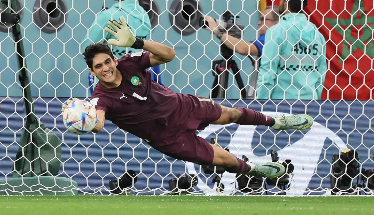 Kiper Maroko Yassine Bounou membelokkan tendangan penalti dari gelandang Spanyol Sergio Busquets pada babak 16 besar Piala Dunia 2022 di Education City Stadium, Al Rayyan, Rabu (6/12/2022) dini hari WIB. Bono tercatat sebagai kiper asal Afrika pertama dan satu-satunya yang mampu menepis dua tendangan dalam satu laga adu penalti Piala Dunia. (JACK GUEZ / AFP)