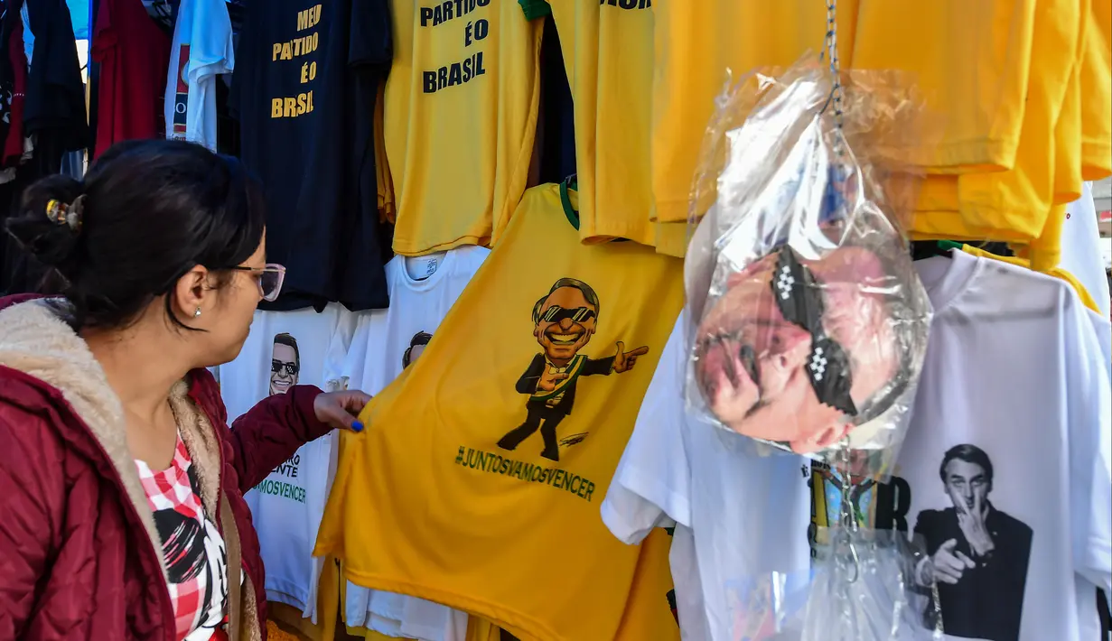 Seorang wanita melihat kaus bergambar Capres Brasil, Jair Bolsonaro dari sayap kanan di sebuah toko pinggir jalan yang populer di Sao Paulo, 8 Oktober 2018. Bolsonaro unggul dalam penghitungan suara pemilu putaran pertama. (AFP/NELSON ALMEIDA)