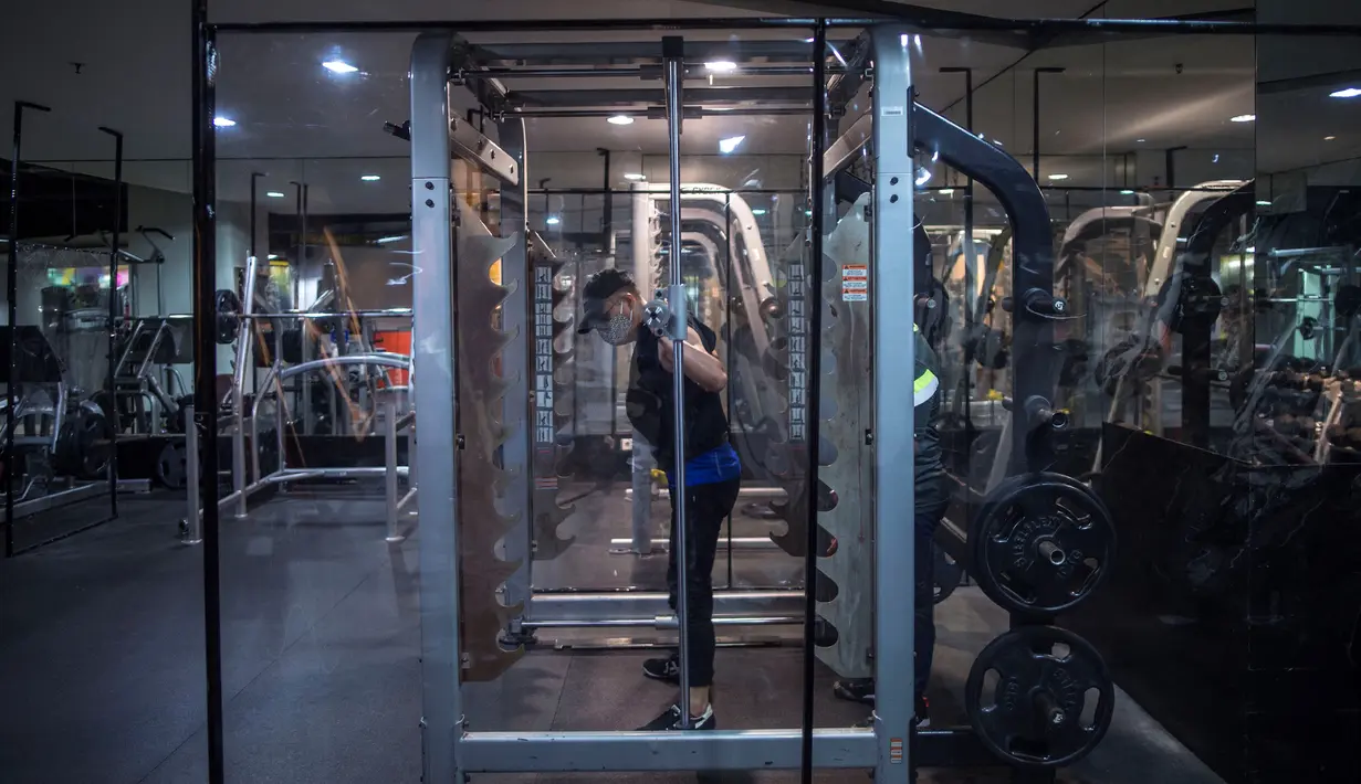 Orang-orang berolahraga dengan plastik penyekat untuk membatasi jarak antar pengunjung di sebuah tempat gym di Surabaya, Rabu (21/10/2020). Pusat kebugaran itu dibuka dengan menerapkan protokol kesehatan sebagai pencegahan COVID-19. (Juni Kriswanto / AFP)
