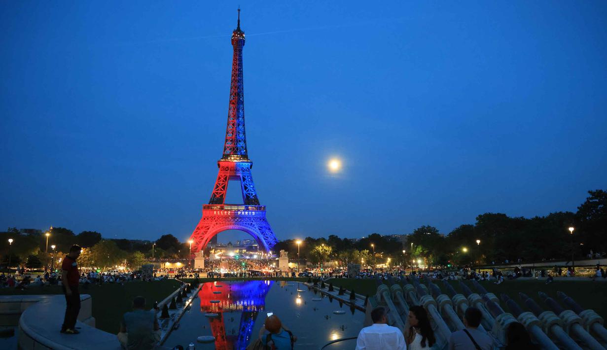 Orang-orang memandang Menara Eiffel yang diterangi cahaya warna-warna khas, dengan pesan bertuliskan "Allez Paris" ("Ayo, Paris"), pada malam menjelang pertandingan final Liga Champions 2025/2026 antara Paris Saint-Germain (PSG) dan Arsenal, Kamis 29 Mei 2026. (Ludovic MARIN/AFP)