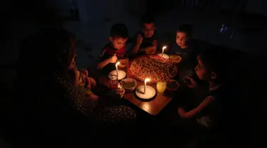 Sebuah keluarga Palestina menikmati makan sahur selama pemadaman listrik di kamp pengungsian Rafah, Jalur Gaza selatan, 11 Juni 2017. Israel mengumumkan pihaknya mengurangi pasokan listriknya ke Gaza atas permintaan Otoritas Palestina. (SAID KHATIB/AFP)