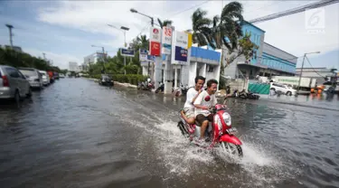 Dua orang remaja mengendarai motor melintasi banjir rob di kawasan Muara Baru, Jakarta, Rabu (6/11). Banjir Rob akibat laut pasang ini, membuat sejumlah aktivitas warga terganggu. Termasuk aktivitas di pasar ikan terhenti. (Liputan6.com/Faizal Fanani)