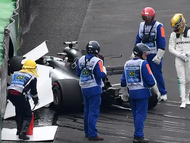 Pembalap Mercedes, Lewis Hamilton (kanan) melihat mobilnya usai menabrak saat kualifikasi F1 GP Brasil di sirkuit Interlagos di Sao Paulo, Brasil (11/11). Mobil Hamilton itu hancur sehingga bendera merah harus berkibar. (AFP Photo/Nelson Almeida)