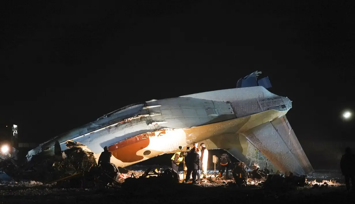 Pekerja darurat bekerja di samping pesawat Antonov An-26 yang jatuh di Bandara Almaty, Kazakhstan, Sabtu (13/3/2021). Saat terjatuh, gumpalan asap mengepul dari lokasi kecelakaan. (AP Photo/Vladimir Tretyakov)