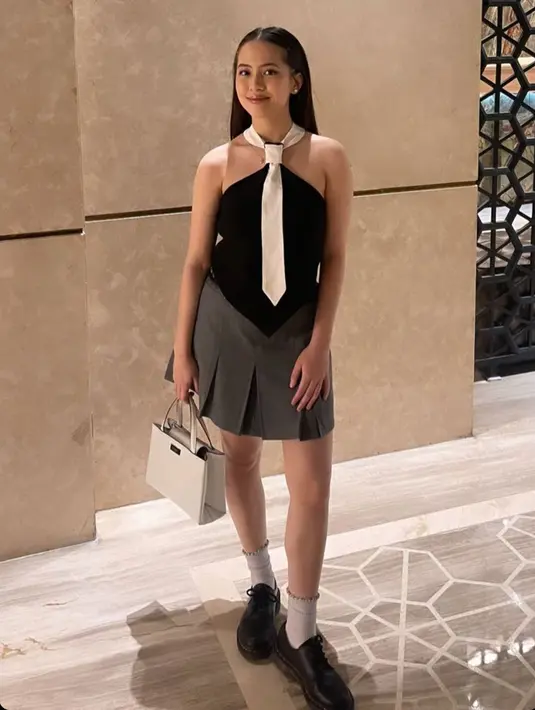 Zara Adhisty tampil mengenakan atasan hitam dengan kerah putih seperti dasi, dipadukan mini skirt dan sepatu model oxford dengan kaos kaki putih serasi dengan hand bagnya. [@zaraadhsty]