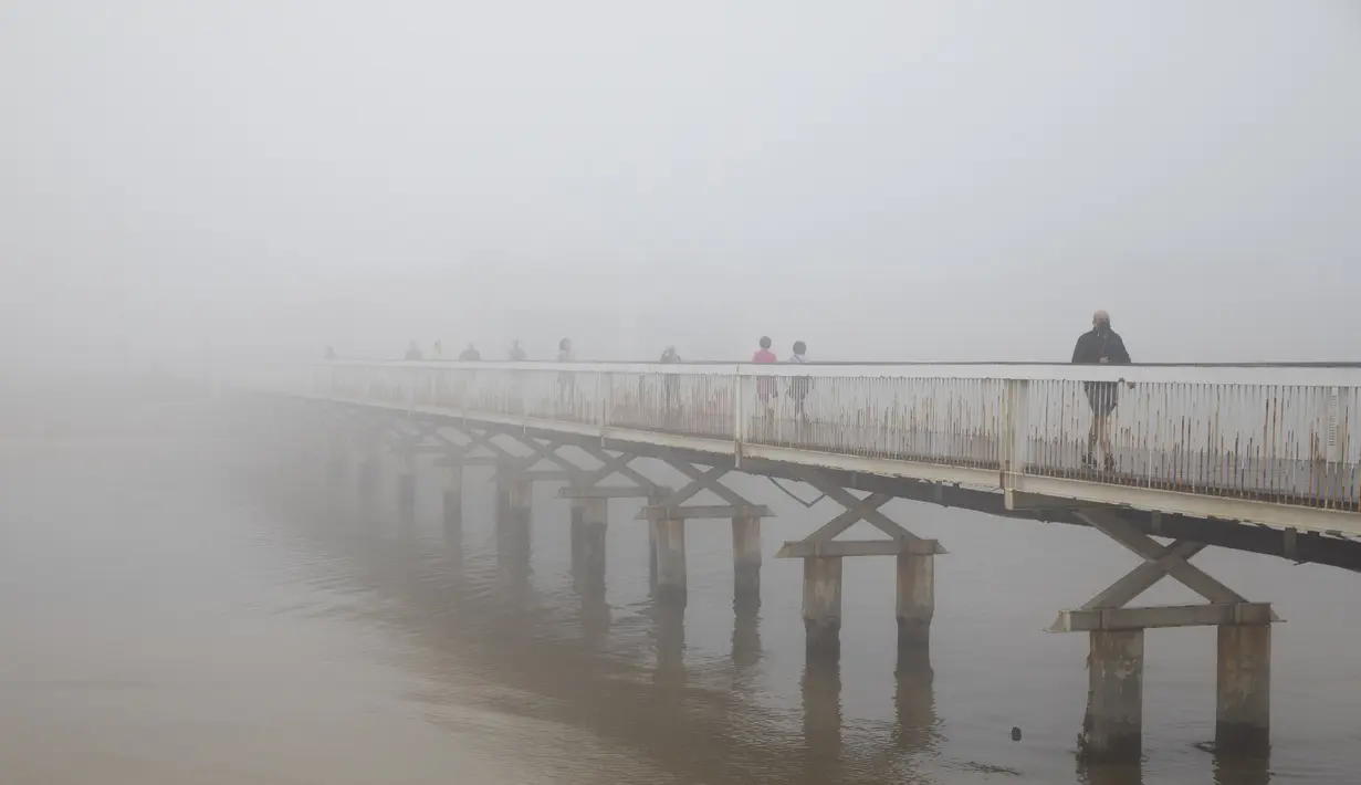 Pejalan kaki menyeberangi jembatan saat hari berkabut di Tel Aviv, Israel, Rabu (6/1/2021). Kabut yang cukup tebal tersebut disebabkan oleh udara yang mengalir ke darat dari laut, menyebabkan kelembaban meningkat di dataran pantai dan daerah lainnya. (AP Photo/Oded Balilty)