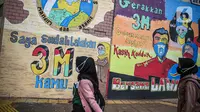 Pejalan kaki melintas dekat lukisan mural melawan COVID-19 di Kawasan Cikokol, Cawang, Jakarta, Minggu (4/10/2020).  Mural masih dianggap menjadi sarana edukasi kesehatan yang tepat bagi warga untuk menjaga diri dari penularan virus Covid 19. (Liputan6.com/Faizal Fanani)