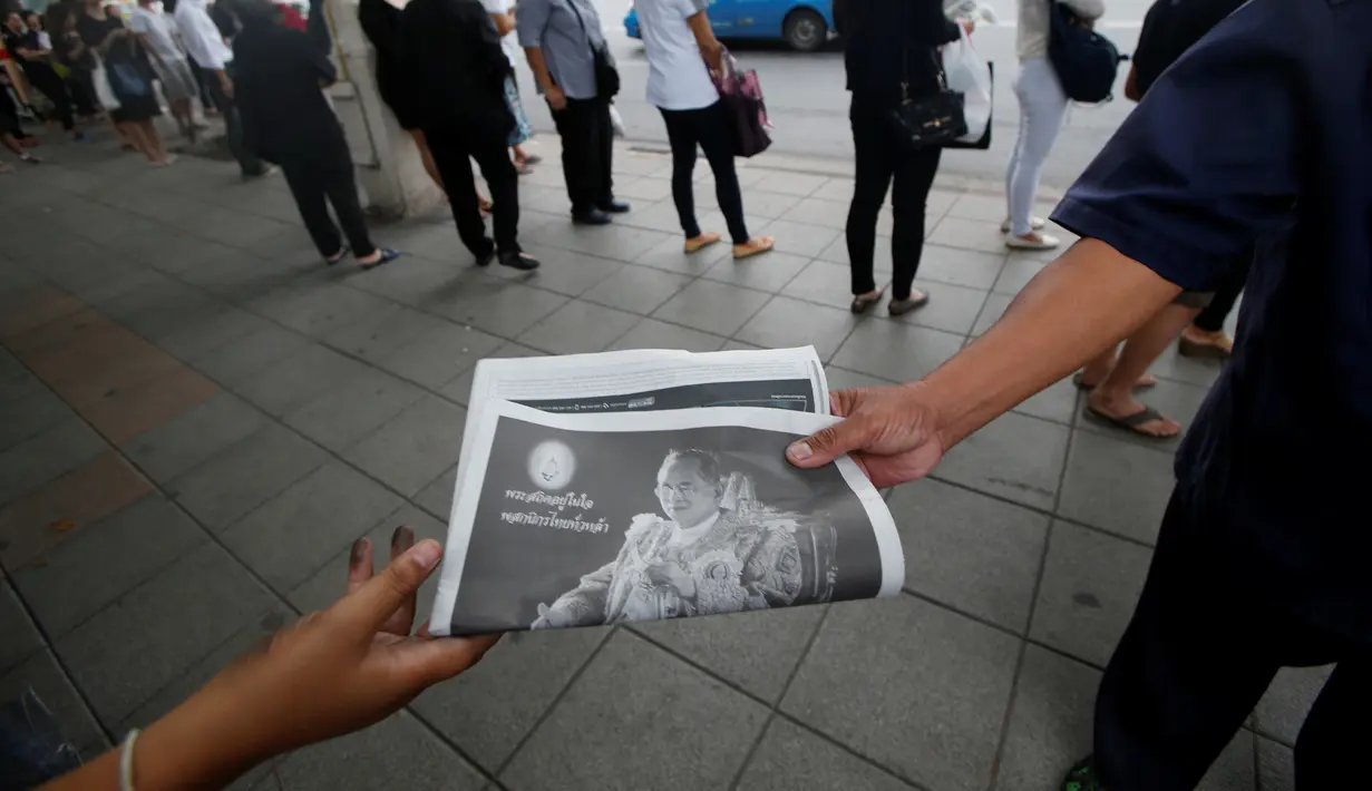 Warga membawa surat kabar berisi berita wafatnya Raja Thailand Bhumibol Adulyadej di Bangkok, Jumat (14/10). Hingga akhir hayatnya, Raja Bhumibol Adulyadej merupakan raja yang paling lama berkuasa di dunia. (Reuters/Edgar Su)