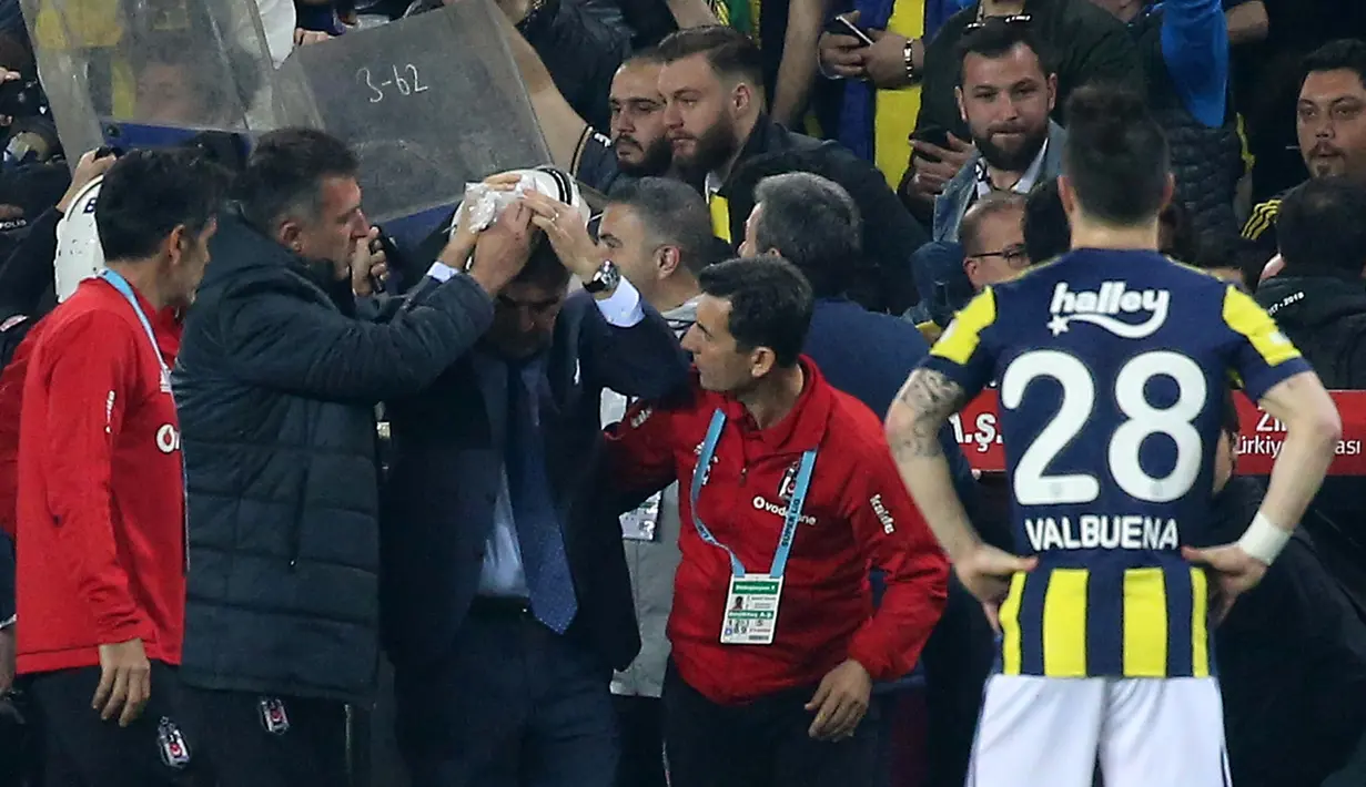 Pelatih Besiktas, Senol Gunes memegangi kepalanya setelah terkena lemparan benda tajam dari tribun penonton pada semifinal Piala Turki melawan Fenerbahce di Istanbul, Kamis (19/4). Insiden di menit ke-58  ini membuat pertandingan terpaksa ditunda. (AFP)
