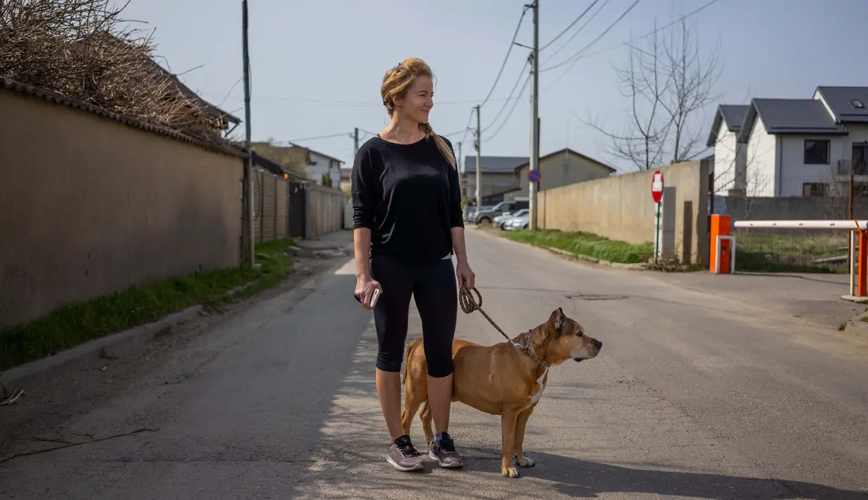 Silvia Rad (34) berpose dengan anjingnya Sa'id (12) saat perjalanan di Bucharest (28/3/2020). Undang-undang militer, yang disahkan pemerintah Rumania untuk mengurangi penyebaran virus corona, menyatakan berjalan bersama anjing adalah salah satu  kegiatan yang masih diizinkan. (AFP/Andrei Pungovschi)