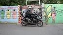 Pengendara sepeda motor melintas di sisi tembok yang terdapat lukisan mural di kawasan Kramat Jati, Jakarta, Rabu (4/4). Mural-mural tersebut mengandung pesan kebersihan, bahaya narkoba hingga pencegahan kekerasan. (Liputan6.com/Herman Zakharia)