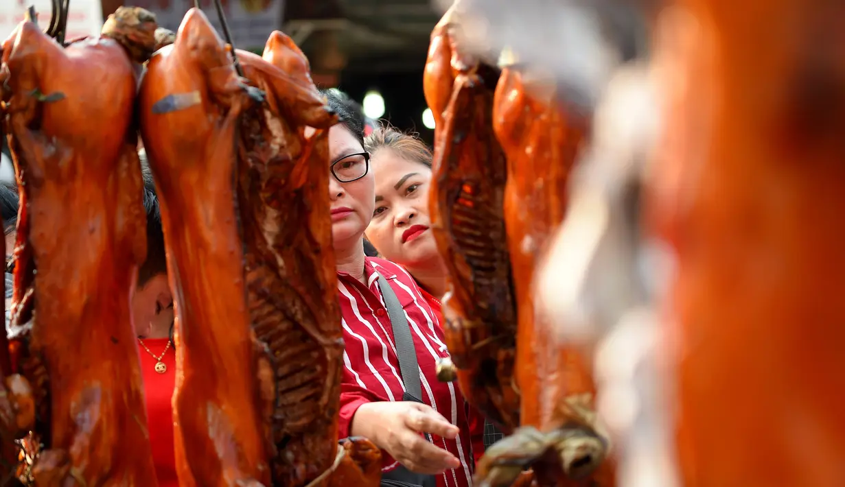 <p>Seorang wanita melihat babi panggang di pasar di Phnom Penh, Kamboja (4/2). Menyambut Tahun Baru Imlek, warga Kamboja mempersiapkan daging babi panggang untuk sajian makan. (AFP Photo/Tang Chhin Sothy)</p>