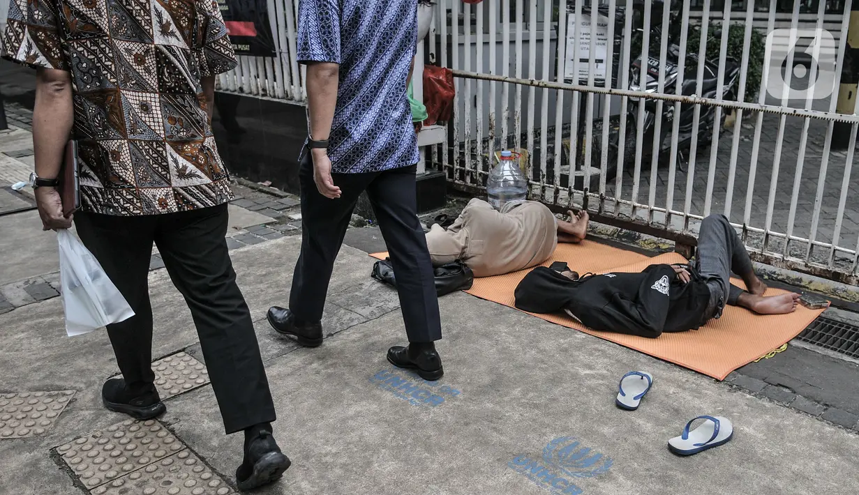 Pekerja melintasi pencari suaka yang tidur di depan Kantor UNHCR Kebon Sirih, Jakarta, Kamis (1/4/2021). Imigran yang terdiri atas orang dewasa hingga anak-anak ini tidur di pinggir jalan menuntut agar proses perpindahan mereka ke negara negara tujuan segera dipercepat. (merdeka.com/Iqbal S Nugroho