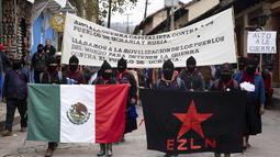 Anggota Tentara Pembebasan Nasional Zapatista (EZLN) memegang bendera Meksiko dan salah satu gerakan selama protes terhadap kapitalisme dan invasi Rusia di Ukraina, di San Cristobal de las Casas, negara bagian Chiapas, Meksiko (13/3/2022). (AP Photo/Isabel Mateos)