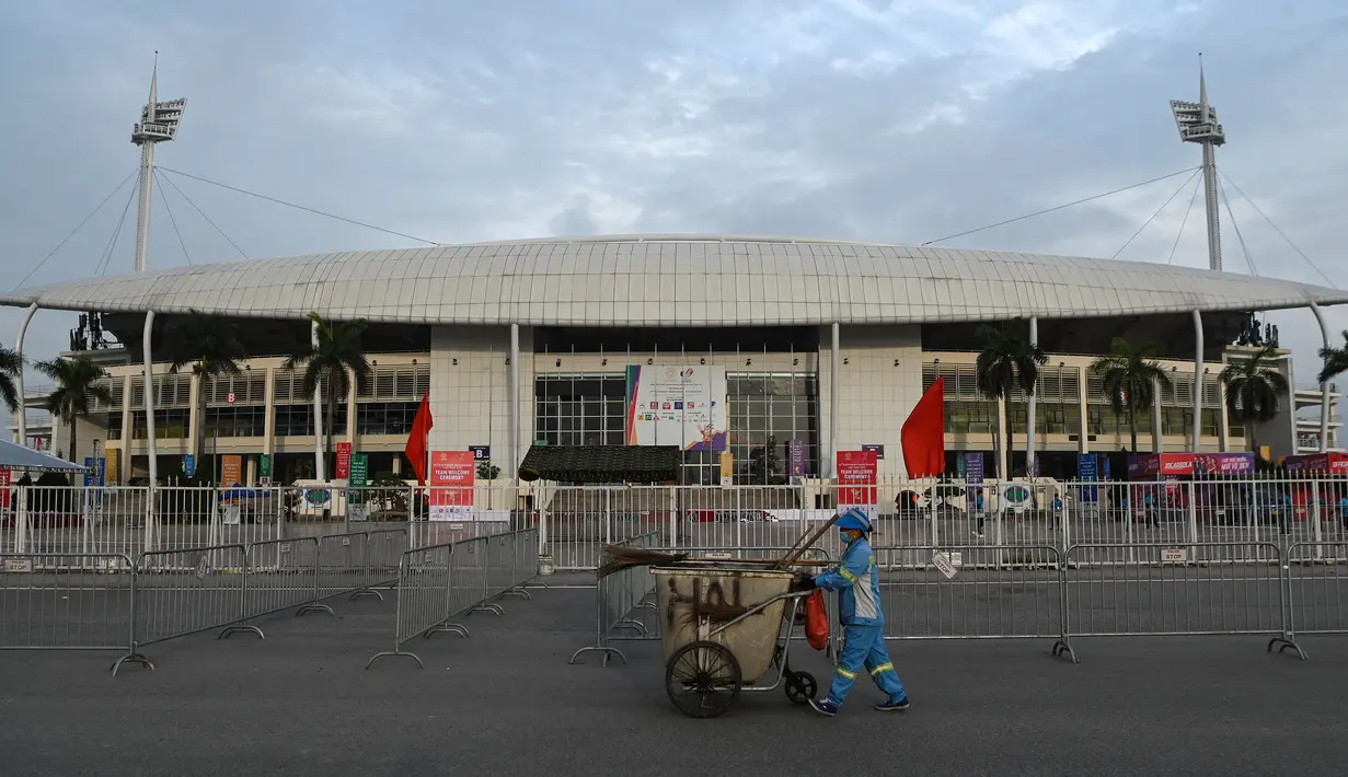 <p>Seorang pekerja mendorong troli di depan Stadion Nasional My Dinh, tempat utama Pesta Olahraga Asia Tenggara (Southeast Asian Games) atau biasa disingkat SEA Games ke-31, sehari sebelum upacara pembukaan di Hanoi, Vietnam, Rabu (11/5/2022). SEA Games 2021 akan dibuka pada 12 Mei 2022 di Stadion My Dinh dengan mempertandingkan 40 cabang olahraga (cabor) dalam 526 nomor. (TANG CHHIN Sothy / AFP)</p>