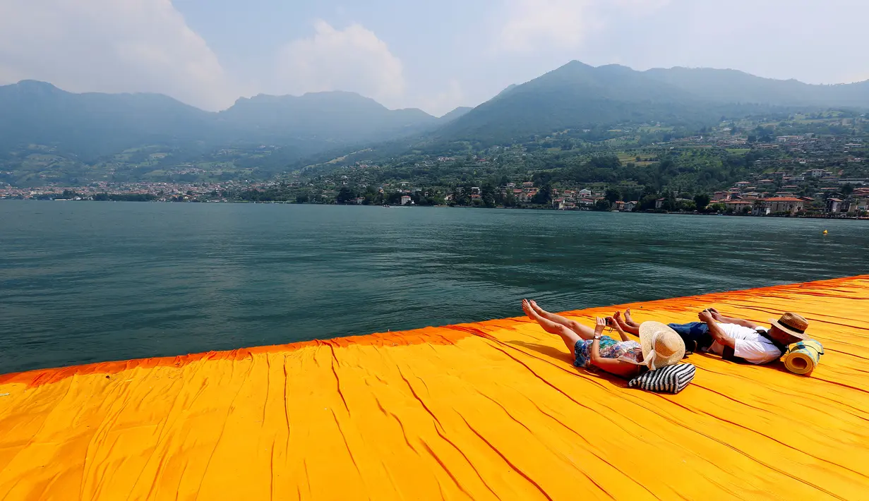 Dua wisatawan bersantai di atas seni instalasi 'The Floating Piers' sambil melihat landscape pemandangan bukti dan pegunungan di utara Italia karya Christo Vladimirov Javacheff di Danau Iseo, Italia utara, (24/6). (REUTERS/Stefano Rellandini)