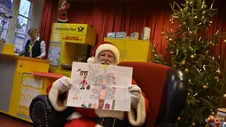 Pria berkostum Sinterklas menunjukkan hadiah lukisan dari seorang anak di Kantor Pos Natal di Himmelpfort, Jerman, 19 Desember 2018. Anak-anak di seluruh dunia mulai mengirim surat berisi permohonan kepada sinterklas di kantor pos itu (Tobias SCHWARZ/AFP)