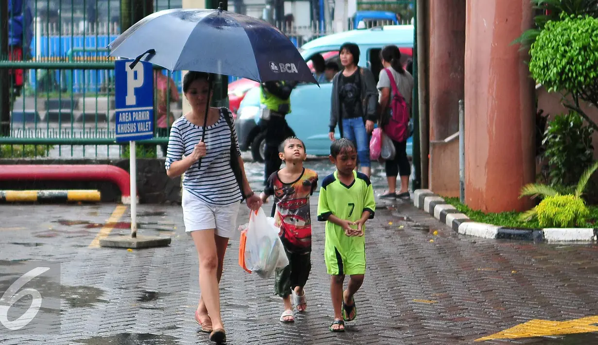 Dua pengojek payung cilik mengikuti  wanita yang memakai jasa ojek payung mereka di Jakarta, Selasa (1/11). Musim hujan membawa berkah bagi anak-anak tersebut karena bisa mendapatkan rezeki lebih dari jasa ojek payung. (Liputan6.com/Angga Yuniar)