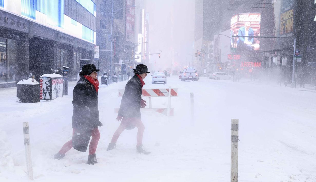 Sedikitnya 21 negara bagian telah menetapkan status darurat, memberi kewenangan tambahan kepada pemerintah lokal untuk menutup fasilitas umum, mengerahkan sumber daya, dan meminta bantuan federal bila diperlukan. Tampak dalam foto, orang-orang berjalan melintasi Sixth Avenue saat salju turun di Kota New York pada 25 Januari 2026. (CHARLY TRIBALLEAU/AFP)