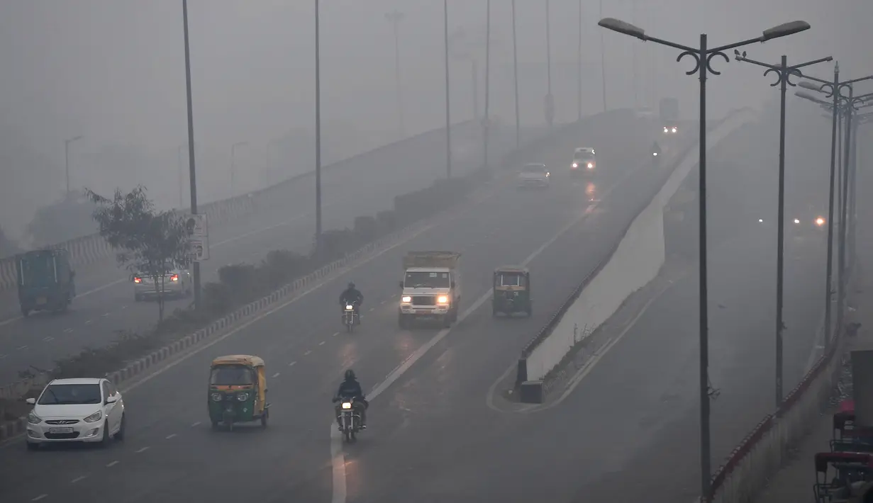 Sejumlah kendaraan melintas di sepanjang jalan di tengah kabut tebal di New Delhi (25/12). India ditetapkan darurat polusi udara. Kualitas udara yang semakin buruk dan kabut beracun menyelimuti. (AFP Photo/Prakash Singh)