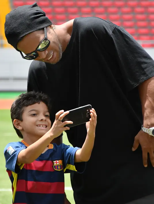Eks Striker Barcelona, Ronaldinho foto bersama dengan seorang anak sebelum pertandingan persahabatan melawan mantan pemain Kosta Rika di Stadion Nasional di San Jose, (4/8). (AFP Photo/Ezequiel Becerra)