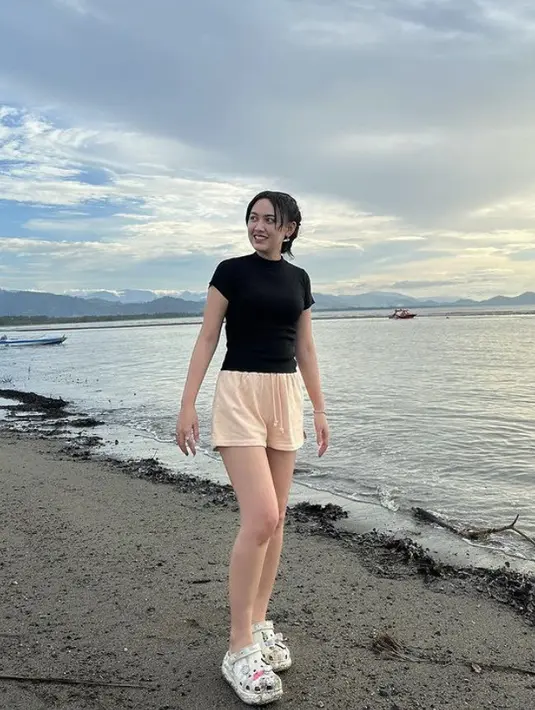 Bermain di pantai, Happy Asmara tampil dengan atasan kaos hitam ketat dipadukan celana pendek warna peach dan sandal karet putihnya.  (@happy_asmara77)