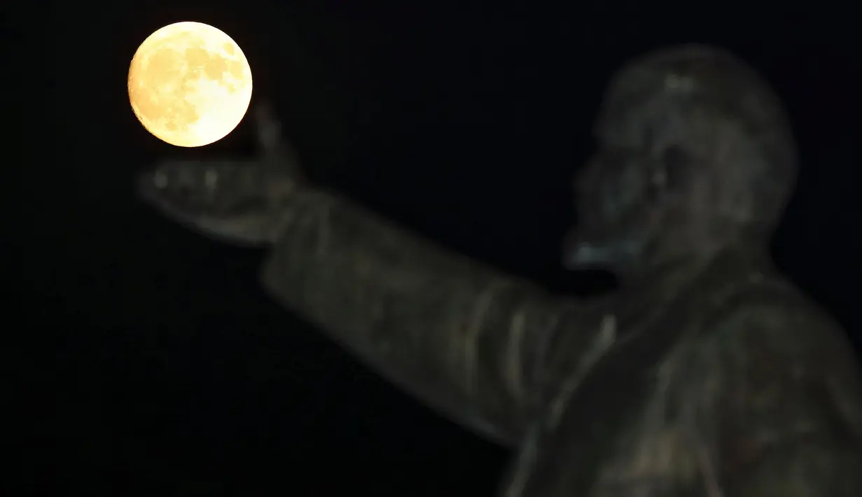 Supermoon terlihat di balik patung pendiri negara Soviet, Vladimir Lenin di Baikonur, Kazakhstan, (13/11). Fenomena ini merupakan bulan paling besar dan terang dalam kurun 70 tahun terakhir. (REUTERS/Shamil Zhumatov)