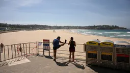 Orang-orang memandangi Pantai Bondi yang kosong setelah ditutup oleh pihak berwenang di Sydney, Minggu (22/3/2020). Otoritas Australia menutup Bondi Beach  lantaran orang-orang mengabaikan larangan tidak berkumpul dalam jumlah besar untuk menekan penyebaran virus corona. (PETER PARKS/AFP)