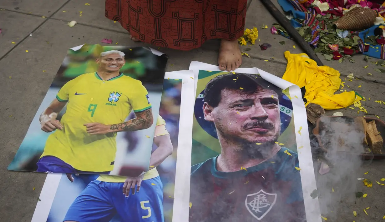 Seorang dukun Peru berdiri di dekat foto pemain sepak bola Brasil Richarlison, kiri, dan pelatih Brasil Fernando Diniz saat ritual keberuntungan tim nasional di luar Stadion Nasional di Lima, Peru, Senin, 11 September 2023. (AP Photo/Martin Mejia)
