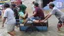 Warga melintasi banjir dengan menaiki ojek gerobak di Ciledug, Tangerang, Banten, Kamis (2/1/2020). Jasa ojek gerobak dipatok dengan harga Rp 20 ribu untuk orang dan Rp 50 ribu untuk motor. (Liputan6.com/Angga Yuniar)