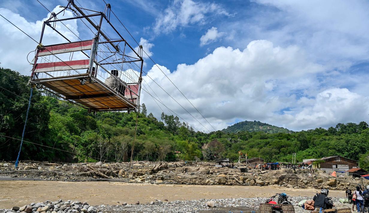 Selain untuk menyeberang, tali sling juga dipakai mengangkut hasil panen seperti durian, cabai, kopi, hingga beras menuju pasar. Tampak dalam foto, warga menggunakan tali untuk menyeberangi sungai setelah banjir bandang yang menghancurkan desa-desa di sekitarnya di Ketol, provinsi Aceh, pada Selasa 6 Januari 2026. (CHAIDEER MAHYUDDIN/AFP)