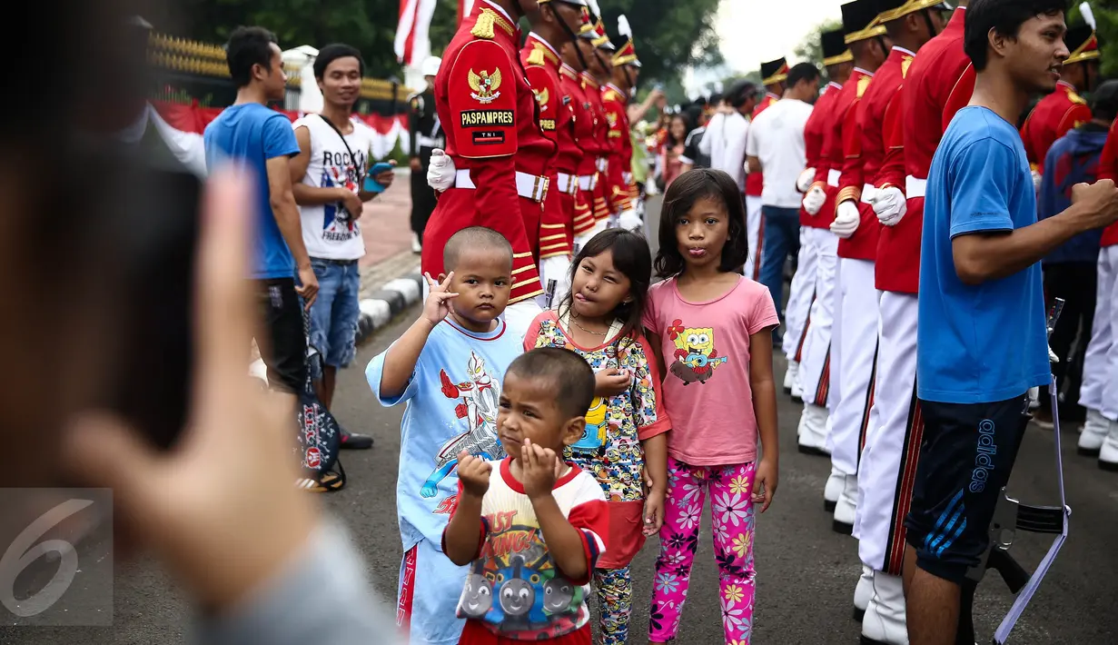 Sejumlah anak berfoto dengan latar belakang anggota Paspampres yang melakukan prosesi pergantian jaga Istana Kepresiden, di depan Istana Merdeka, Minggu (28/8). Seremoni pergantian pasukan ini mengundang perhatian warga. (Liputan6.com/Faizal Fanani)