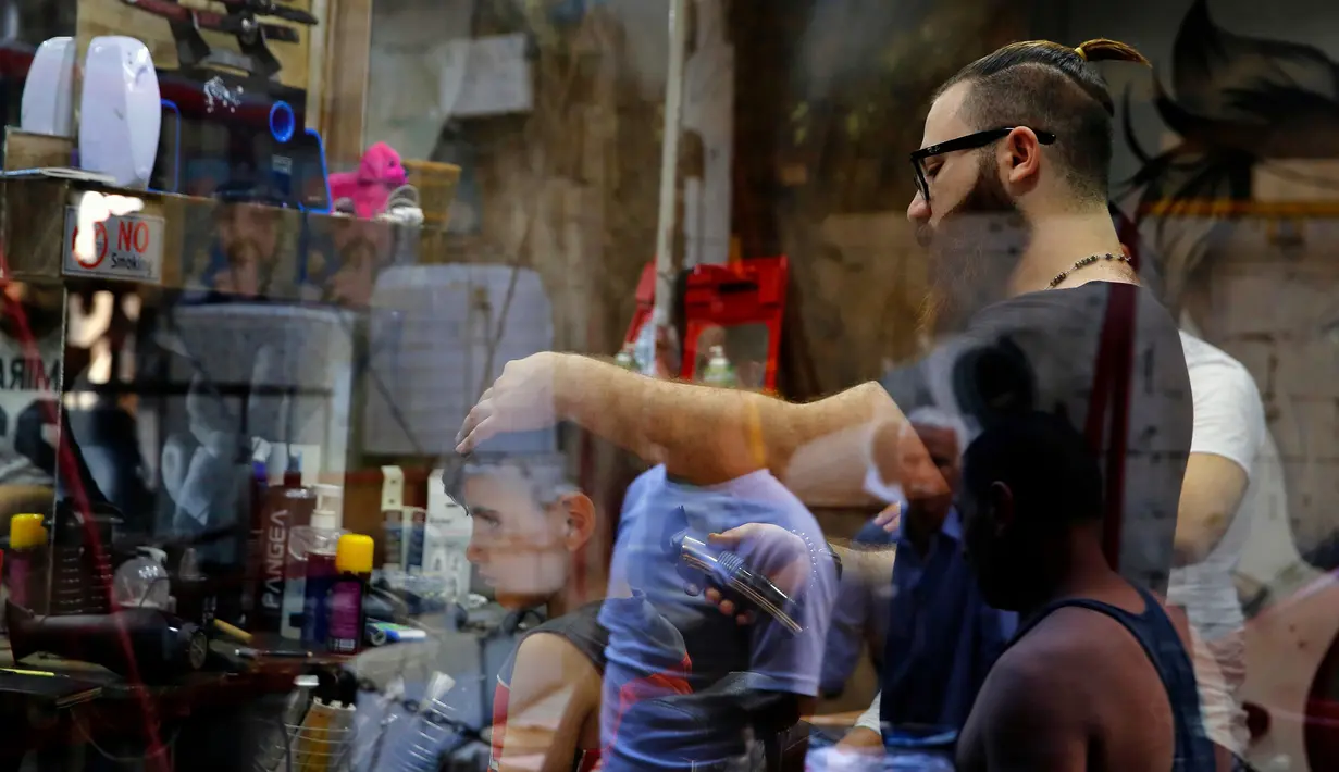 Muhannad Khaled Omar memotong rambut pelanggannya di Burj al-Barajneh, Lebanon (14/7). (AP Photo / Bilal Hussein)