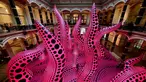 Pengunjung berjalan melewati instalasi seni berjudul 'A bouquet of love I saw in the universe' karya seniman kontemporer Jepang Yayoi Kusama dalam pameran Yayoi Kusama: A Retrospective di Atrium Martin Gropius Bau, Berlin, Jerman, Selasa (19/5/2021). (John MACDOUGALL/AFP)