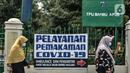 Warga melintas di depan kompleks makam protokol Covid-19 di TPU Bambu Apus, Jakarta, Selasa (2/3/2021). TPU Bambu Apus kini tidak lagi menampung pemakaman jenazah protokol Covid-19 akibat lahan di dua blok sudah penuh dan dialihkan ke TPU Srengseng Sawah. (merdeka.com/Iqbal S Nugroho)