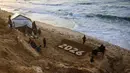 Sementara itu, sekitar 1,9 juta orang atau setidaknya 90% dari total populasi Gaza telah mengungsi setidaknya satu kali sejak perang meletus pada Oktober 2023 lalu. Tampak dalam foto, anak-anak berdiri di samping patung pasir karya seniman Yazed Abo Jarad (kanan) yang menggambarkan tahun mendatang di Deir El-Balah, Jalur Gaza tengah pada 30 Desember 2025. (Bashar Taleb/AFP)