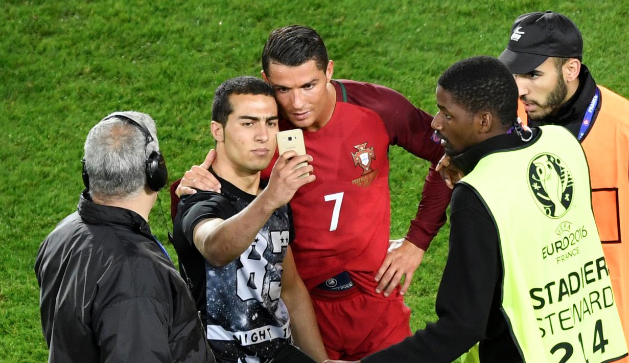Seorang penggemar masuk lapangan dan mengajak berfoto Cristiano Ronaldo seusai laga Portugal melawan Austria pada laga kedua Grup F Piala Eropa 2016di Parc des Princes, Minggu (19/6/2016) dini hari WIB. (AFP/Miguel Medina)