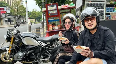 Pasangan Shandy Purnamasari dan Gilang Juragan 99 terlihat santai saat makan bubur ayam kaki lima dengan outfit hitam. Di kepalanya masih menempel helm dan berkaca mata. (FOTO: instagram.com/shandypurnamasari/)