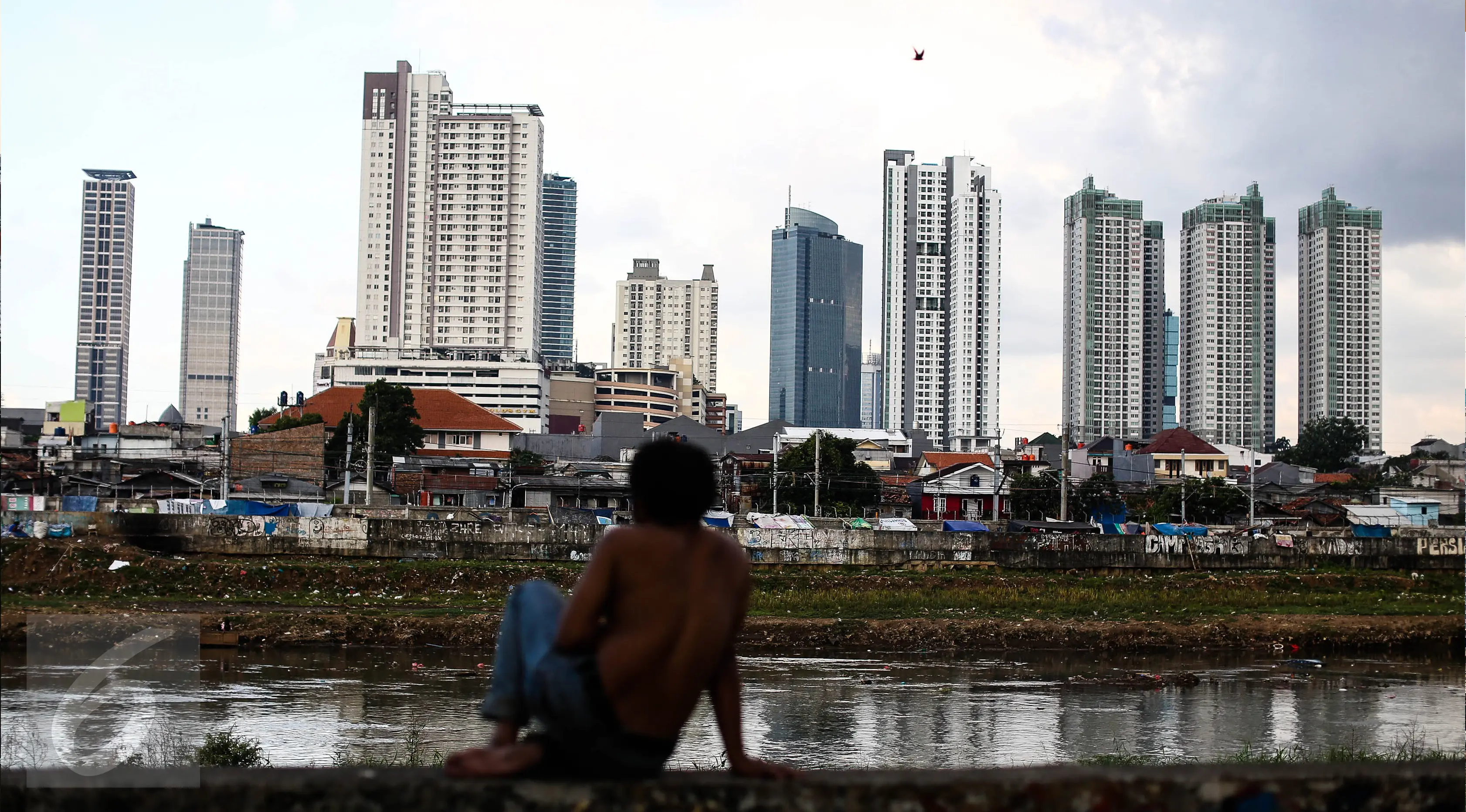 Seorang warga memandangi permukiman kumuh diantara gedung pencakar langit di kawasan Petamburan, Jakarta, Senin (11/7).11 Juli merupakan hari populasi dunia.  (Liputan6.com/Faizal Fanani)