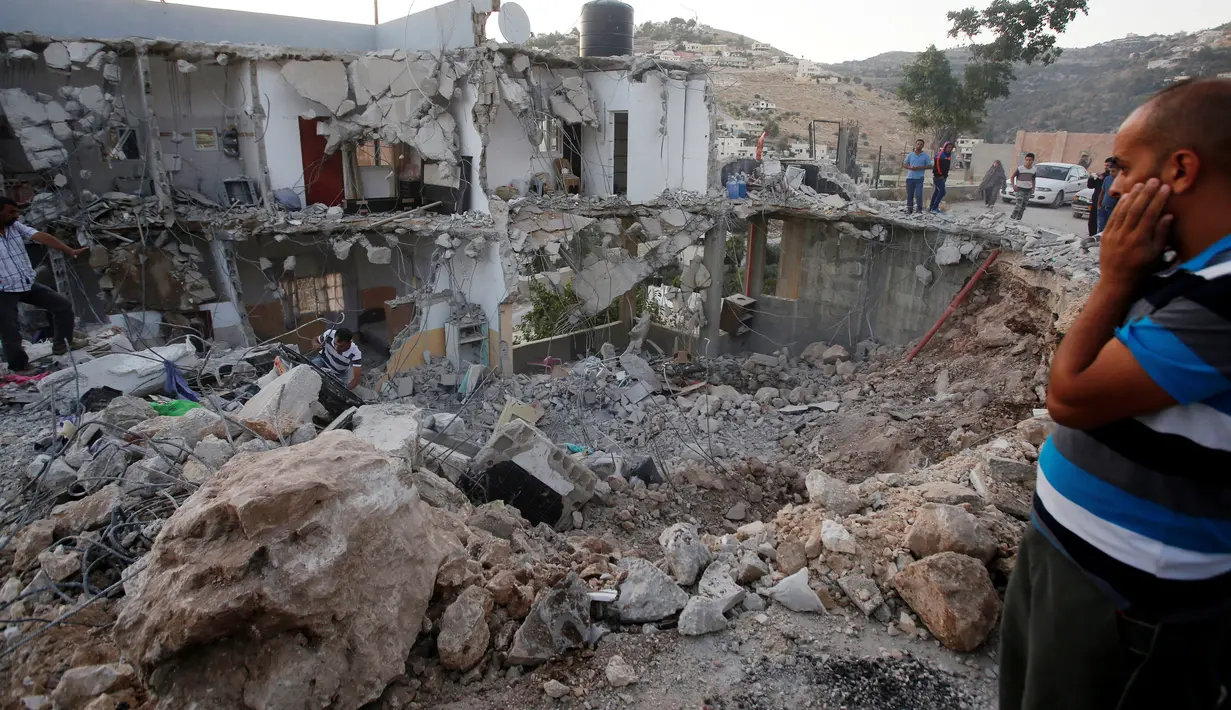 Warga Palestina berkumpul melihat sisa  rumah pejuang Hamas Mohammad al-Fakih yang ditembak mati oleh pasukan Israel di desa Tepi Barat Surif, dekat Hebron, (27/7). Serangan itu menewaskan satu pejuang Hamas, Mohammad Al-Fakih. (REUTERS/Mussa Qawasma)