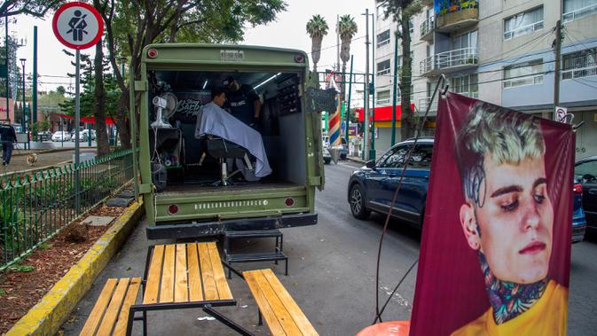 Seorang tukang cukur memotong rambut pelanggan di mobil van atau truck yang diubah menjadi barbershop di sebuah jalan di tengah pandemi virus corona COVID-19, di Mexico City, pada Minggu (6/9/2020). (Photo by CLAUDIO CRUZ / AFP)