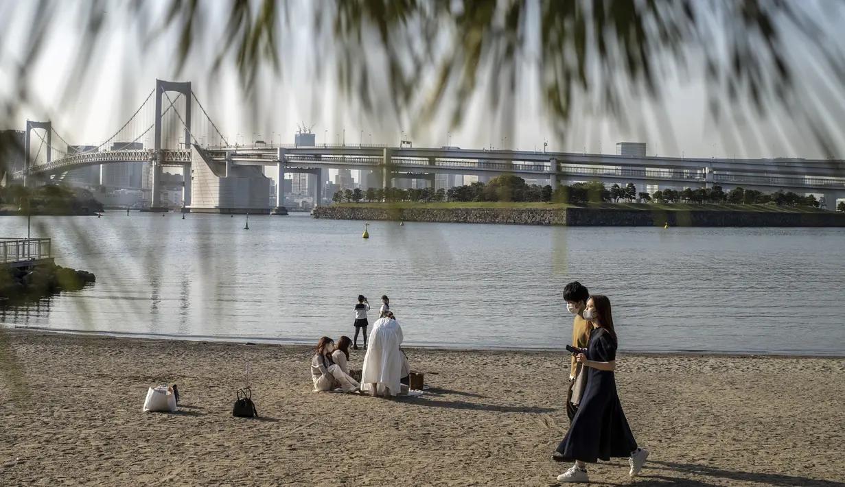 Orang-orang berjalan pada hari yang cerah di tepi teluk di daerah Odaiba Tokyo (12/4/2022). Para pengunjung biasanya datang ke Seaside Park untuk menikmati pemandangan Gunung Fuji dari bianglala Daikanransha dan berinteraksi dengan robot di museum sains Miraikan. (AFP/Charly Triballeau)