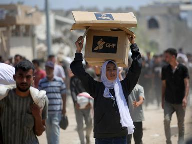 Seorang wanita Palestina membawa bantuan makanan ketika orang-orang kembali ke kamp pengungsi Nuseirat dari titik distribusi Yayasan Kemanusiaan Gaza yang didukung oleh Amerika Serikat (AS) di dekat koridor Netsarim, Jalur Gaza tengah, pada 27 Juli 2025. (Eyad BABA/AFP)