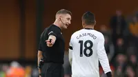 Pemain Manchester United, Casemiro (kanan) diberikan peringatan oleh wasit&nbsp;Robert Jones saatpertandingan lanjutan Liga Inggris 2022/2023 melawan Wolverhampton Wanderers&nbsp;yang berlangsung di&nbsp;Molineux stadium (31/12/2022). (AFP/Adrian Dennis)