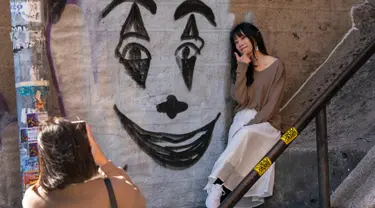 Seorang wanita berpose dekat lukisan wajah Joker di tangga di kawasan Bronx, New York, 23 Oktober 2019. Tangga yang terletak tepat di West 167th Street itu menjadi buruan wisatawan, terutama para penggemar film Joker yang ingin berfoto. (Don Emmert / AFP)