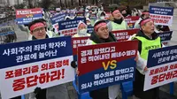 Para dokter memegang plakat bertuliskan "Hentikan Kebijakan Medis Populis!" dalam unjuk rasa memprotes rencana pemerintah menaikkan kuota pendaftaran tahunan di sekolah kedokteran, di dekat kantor kepresidenan di Seoul pada tanggal 21 Februari 2024. (Jung Yeon-je/AFP)
